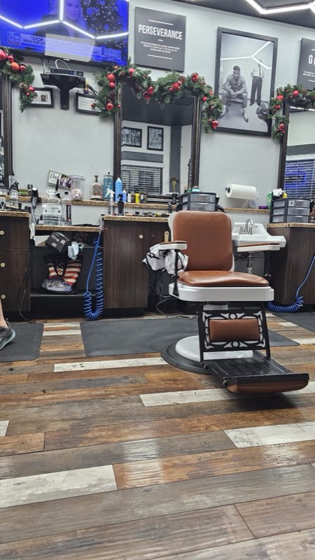 A vintage tan-leather barber chair on a reclaimed-wood floor, mirrors and framed art behind it