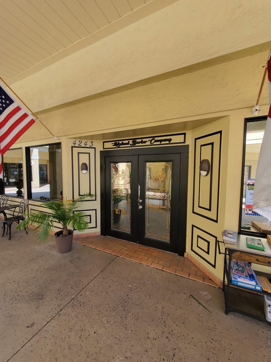 The front doors of Lakeland Barber Company - black double doors with gold lettering, under the shop sign and an American flag